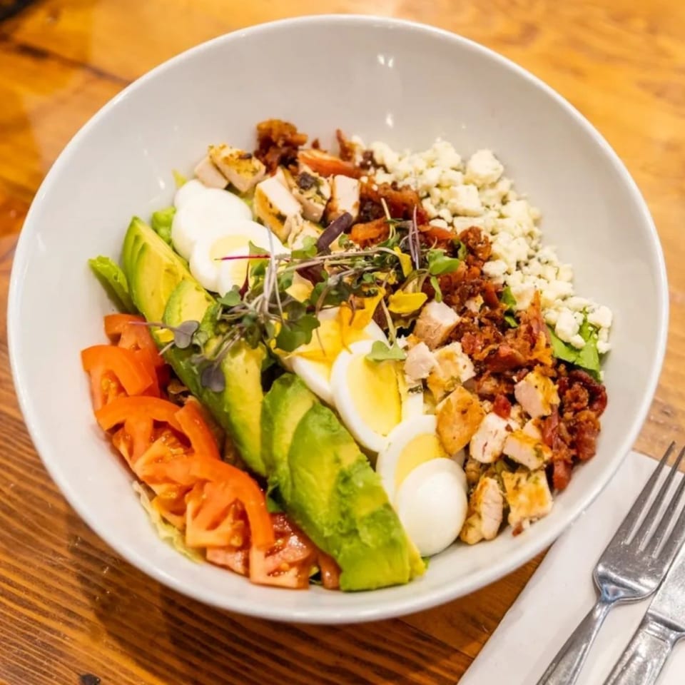 A vibrant Cobb salad with chicken, avocado, tomatoes, eggs, bacon, and blue cheese crumbles.