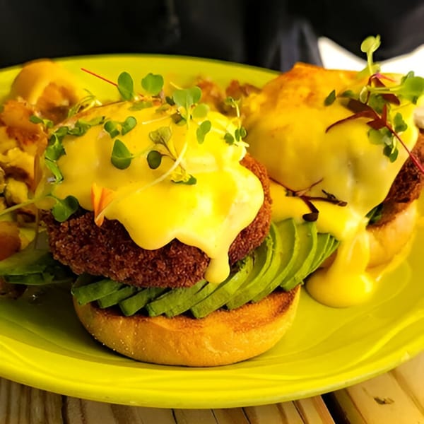 Two eggs benedict with avocado, fried patties, and hollandaise sauce on a bright green plate.