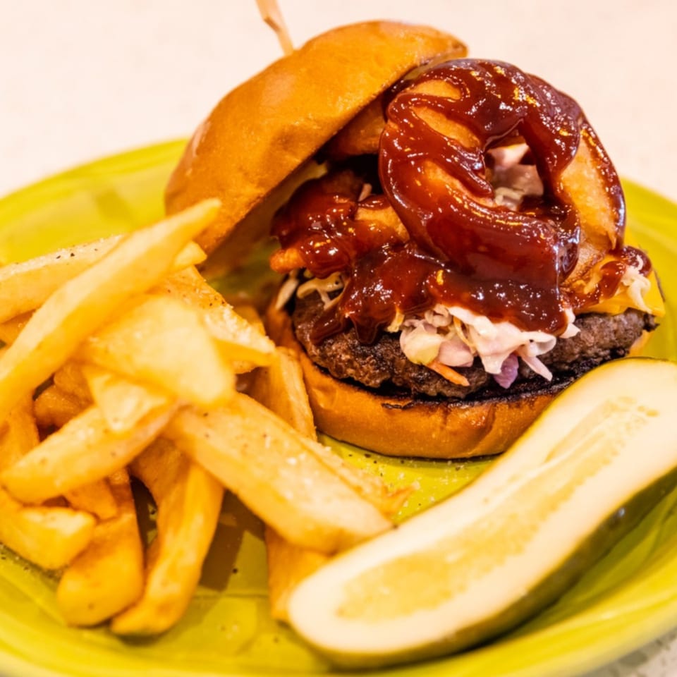 A BBQ burger with onion rings, coleslaw, fries, and a pickle spear on a green plate.