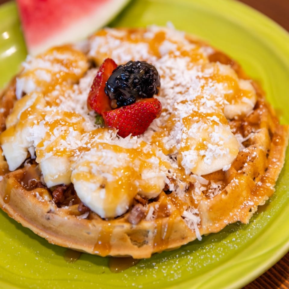 Waffle topped with bananas, strawberries, blackberries, powdered sugar, and syrup on a green plate.